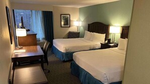 A hotel room with two beds, a desk, a chair, and a window with curtains.