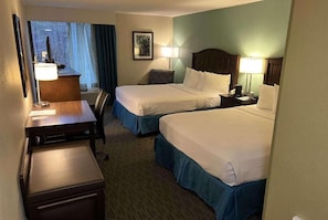 A hotel room with two beds, a desk, a chair, and a window with curtains. - Williamsburg Historic District (Williamsburg)