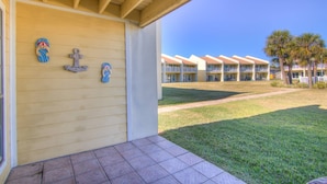A hotel entrance with a covered porch, a tiled patio, and a view of a building with multiple balconies and palm trees. - 3A, Rumrunner Retreat (Destin)