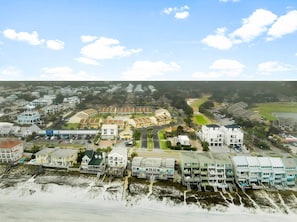 An aerial view of a coastal residential area with beachfront properties, a central commercial building, and a golf course.