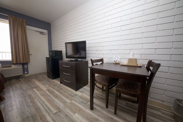 A room with a TV, a small cabinet, a table with chairs, and a white brick wall. - Beach House Inn (Daytona Beach)