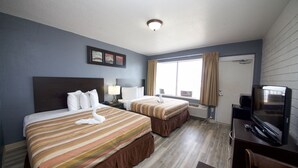 Una habitació d'hotel amb dos llits, un escriptori amb televisió i una finestra amb cortines.