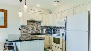 A kitchen with white cabinets, a tiled backsplash, a stainless steel refrigerator, and a bar stool. - 9H, Rhythm & Waves Retreat (Destin)