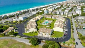 An aerial view of a coastal hotel with multiple buildings, a parking lot, and a beach in the background. - 9H, Rhythm & Waves Retreat (Destin)