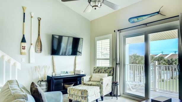 A living room with a TV, paddleboards, and a balcony with a view. - 9H, Rhythm & Waves Retreat (Destin)