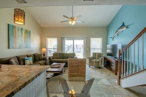 A spacious living area with a large window, a ceiling fan, and a television.