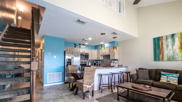 A spacious living area with a kitchen, a staircase, and a large painting on the wall. - 9G, Tan Lines & Good Times (Destin)
