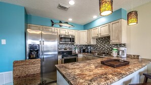 A kitchen with a large island, stainless steel appliances, and a blue accent wall. - 9G, Tan Lines & Good Times (Destin)