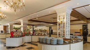 A buffet area with multiple serving stations, a chandelier, and a patterned floor. - Club Felicia Village (Manavgat)