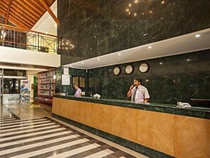 A hotel reception area with a marble reception desk, a second-floor balcony, and a check-in counter.