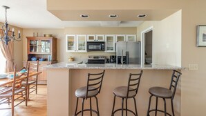 A modern kitchen with a central island, bar stools, and a dining area with wooden chairs. - Bluff Villa 2014 on Dataw Island (Saint Helena Island)