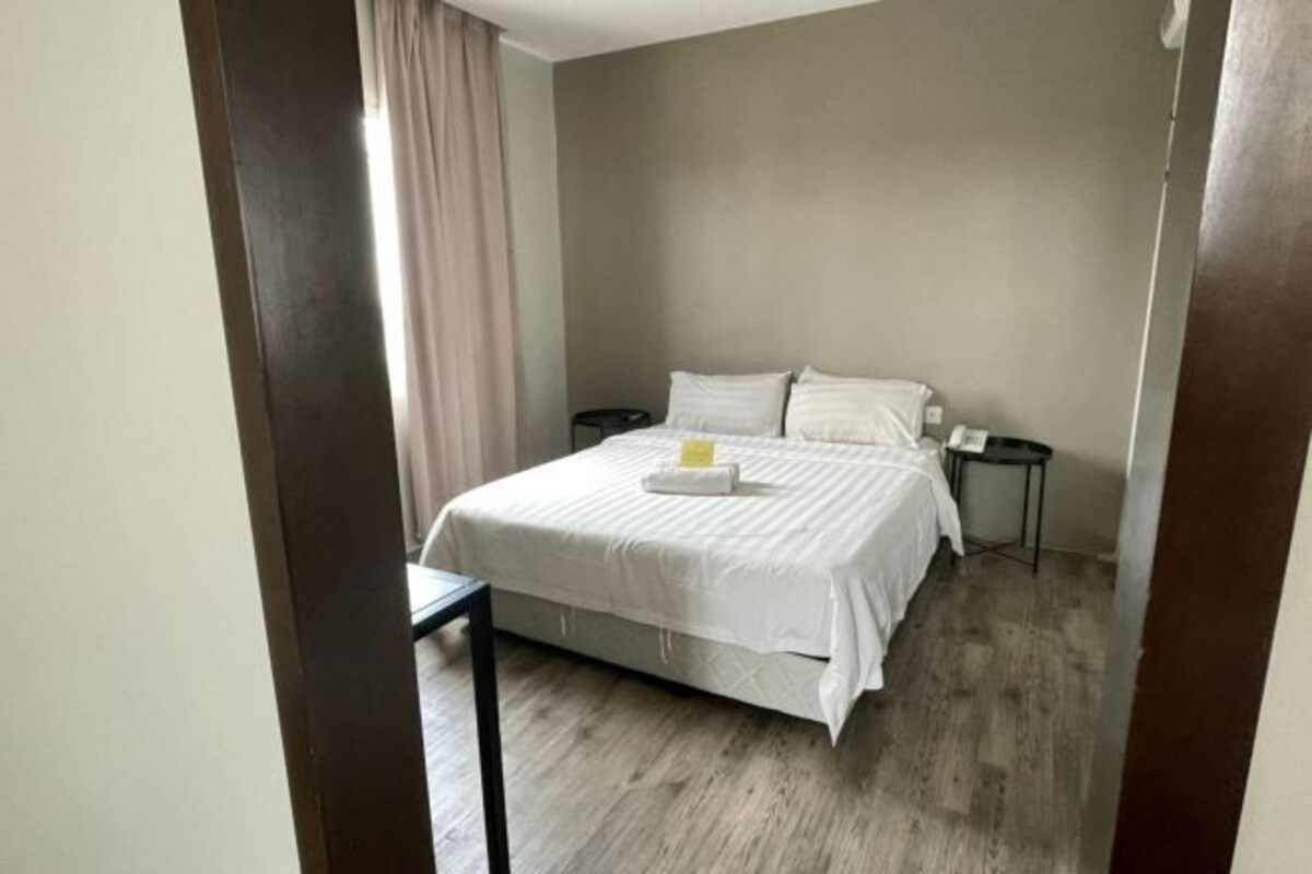 Een hotelkamer met een bed, nachtkastjes, een klein tafeltje en een gordijn.