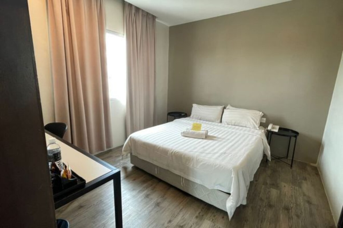 Een hotelkamer met een bed, bureau, stoel, nachtkastje en een raam met gordijnen.