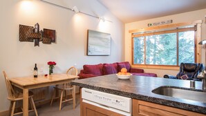 A compact kitchen with a granite countertop, a dishwasher, and a dining area with a wooden table and chairs. - Northstar - Ski Trail Condo (Truckee)