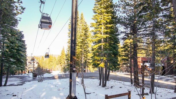 A snow-covered park with a bench, trees, and a cable car. - Northstar - Ski Trail Condo (Truckee)