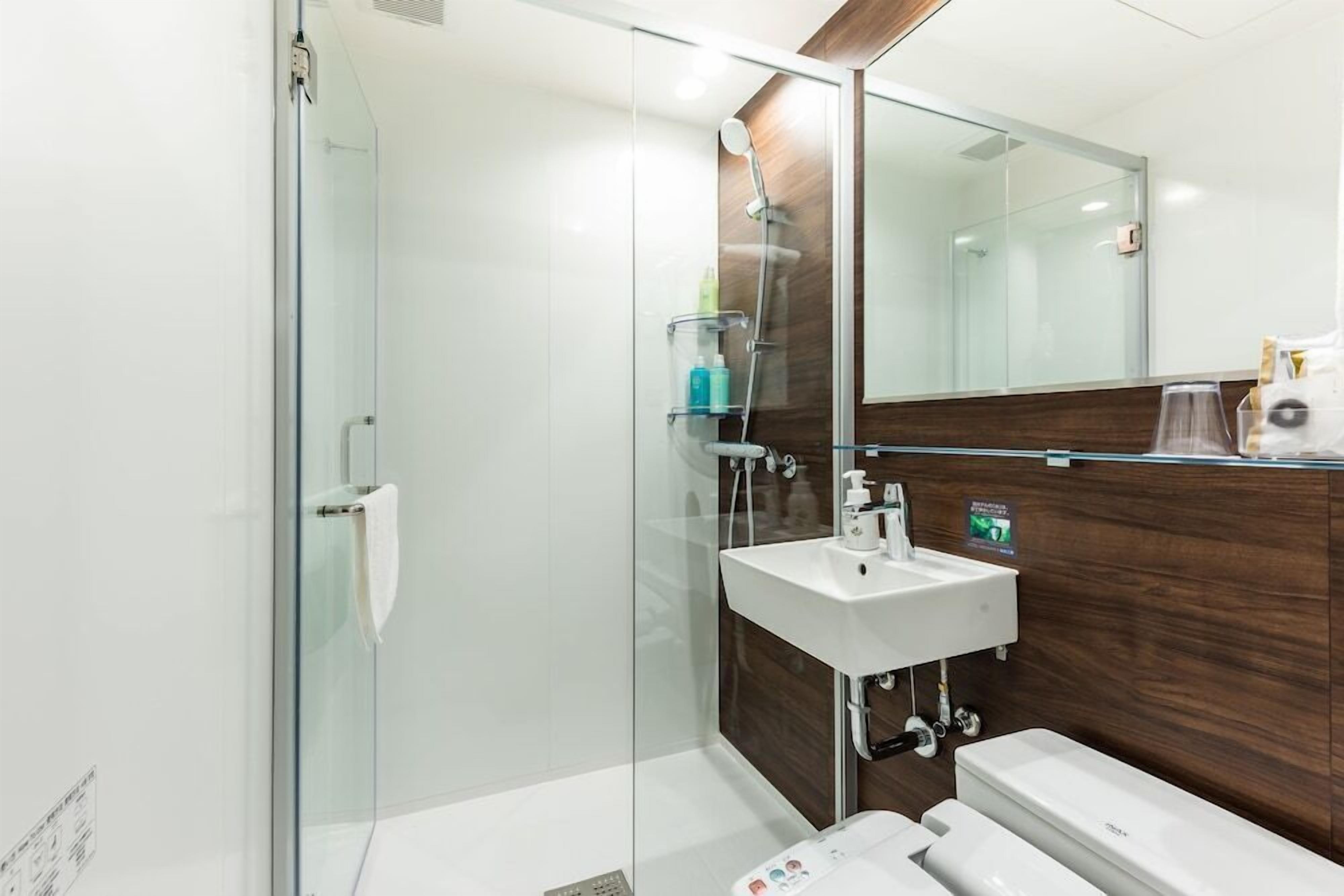 Uma casa de banho moderna com cabine de duche em vidro, uma sanita branca e um espelho.