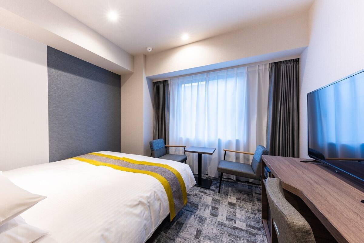 A hotel room with a bed, two chairs, a desk, and a TV.