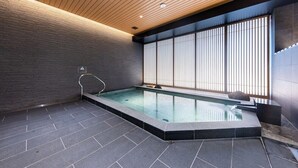 A modern indoor swimming pool with a wooden ceiling, stone walls, and a large window with vertical blinds. - Kazusaya Hotel (Tokyo)