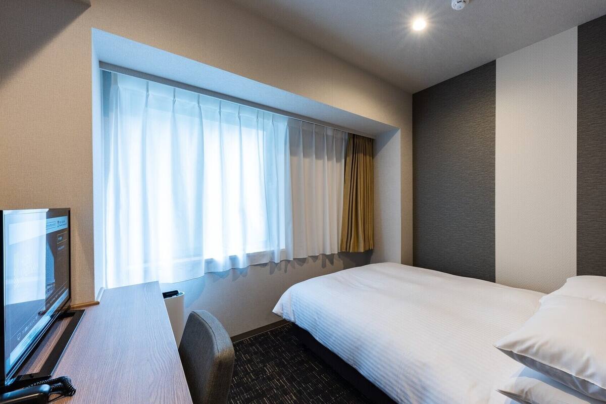A hotel room with a bed, a desk, a TV, and a window with curtains.