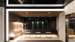 A modern waiting area with a bench seating arrangement, recessed lighting, and a view of the outside. - Kazusaya Hotel (Tokyo)