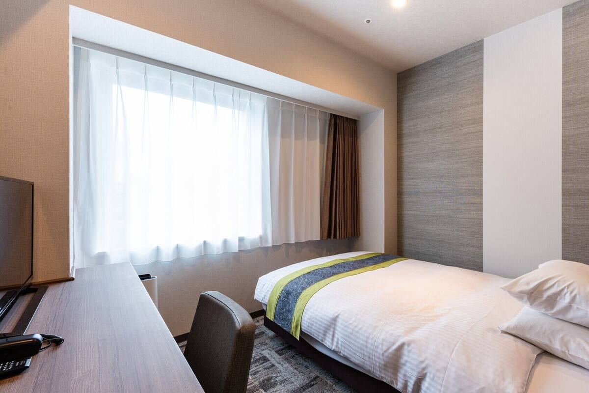 A hotel room with a bed, a desk, and a window with curtains.