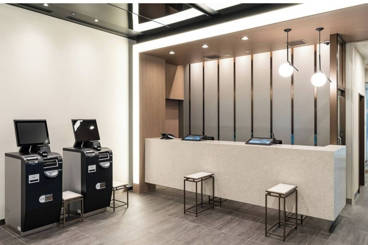 A reception desk with a modern design, two self-service kiosks, and a seating area with stools.