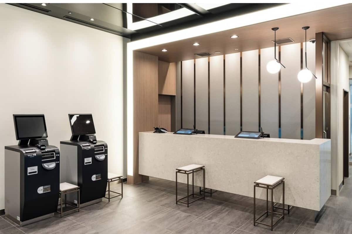 A reception desk with a modern design, two self-service kiosks, and a seating area with stools.