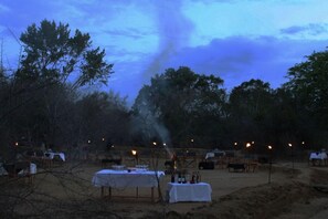 An outdoor dining area with tables and chairs, surrounded by trees and a clear sky. - Big Game Camp - Yala (Kataragama)