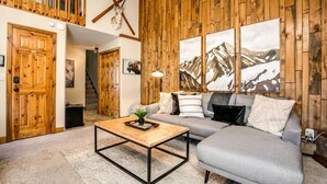 Una sala de estar acogedora con una pared de madera, un sofá gris, una mesita de centro y una escalera que sube.