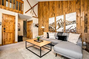 Un salon chaleureux avec un mur en bois, un canapé gris, une table basse et un escalier menant à l’étage.