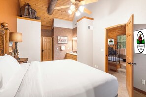 A bedroom with a bed, wooden ceiling, and a ceiling fan. There is a bathroom with a sink and mirror. A door leads to a balcony with a view of the surroundings. - Two Connected Cabins, 4 King Suites and Walk-In Access Just Minutes from Branson's Top Attractions (Branson)