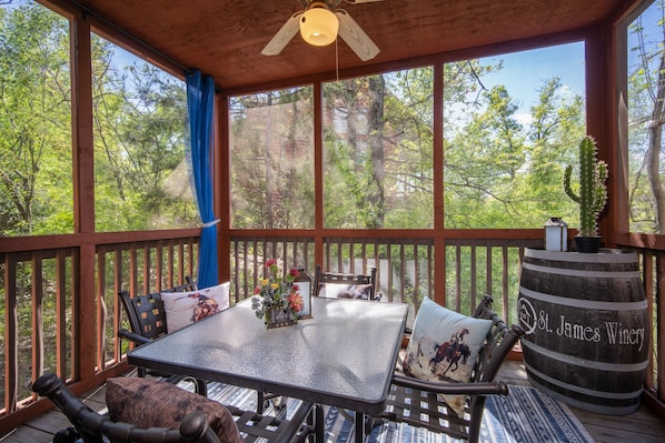A covered outdoor deck with a table and chairs, a wooden barrel labeled "St. James Winery," and a view of trees through large windows. - Two Connected Cabins, 4 King Suites and Walk-In Access Just Minutes from Branson's Top Attractions (Branson)