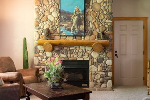 A stone fireplace with a mounted painting, a cactus, and a wooden table with a floral arrangement. - Two Walk-In Connected Cabins in the Heart of Branson, Golf and Ticket Discounts! Sleeps 14 (Branson)