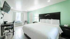 A hotel room with a bed, a desk with a computer, a chair, a TV, and a nightstand with a lamp. - Everglades City Motel - King Hotel Room (Everglades City)