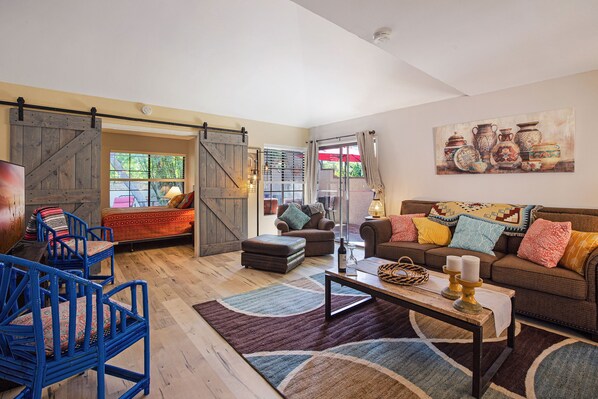 Un salon spacieux avec un grand canapé, une table basse et des fauteuils bleus. On y trouve une porte coulissante de style rustique et un tableau accroché au mur.