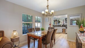 A dining area with a wooden table and chairs, a chandelier, and a view of the kitchen through an open door. - Oasis with 3rd Bedroom/Den, sleeps 6, 3 patios, adult and childrens bikes (Palm Springs)
