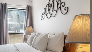 Camera d'albergo con un letto, due lampade ai comodini, una finestra con tende e un elemento decorativo a parete.