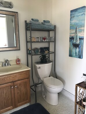 A bathroom with a toilet, sink, and a shelf with decorative items. - The Boathouse (Eureka)