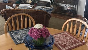 A dining area with a wooden table, chairs, a vase with flowers, a television on the wall, and a decorative wheel. - The Boathouse (Eureka)