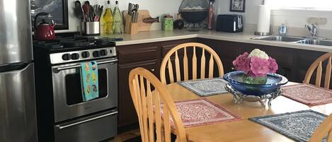 A kitchen with dark wooden cabinets, a stainless steel refrigerator, a stove, and a dining table with four wooden chairs.