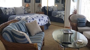 A well-lit room with a bed, two sofas, a glass coffee table, and a ceiling fan. - The Boathouse (Eureka)
