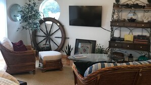 A cozy living room with wicker furniture, a large wheel, a flat-screen TV, and a bookshelf. - The Boathouse (Eureka)