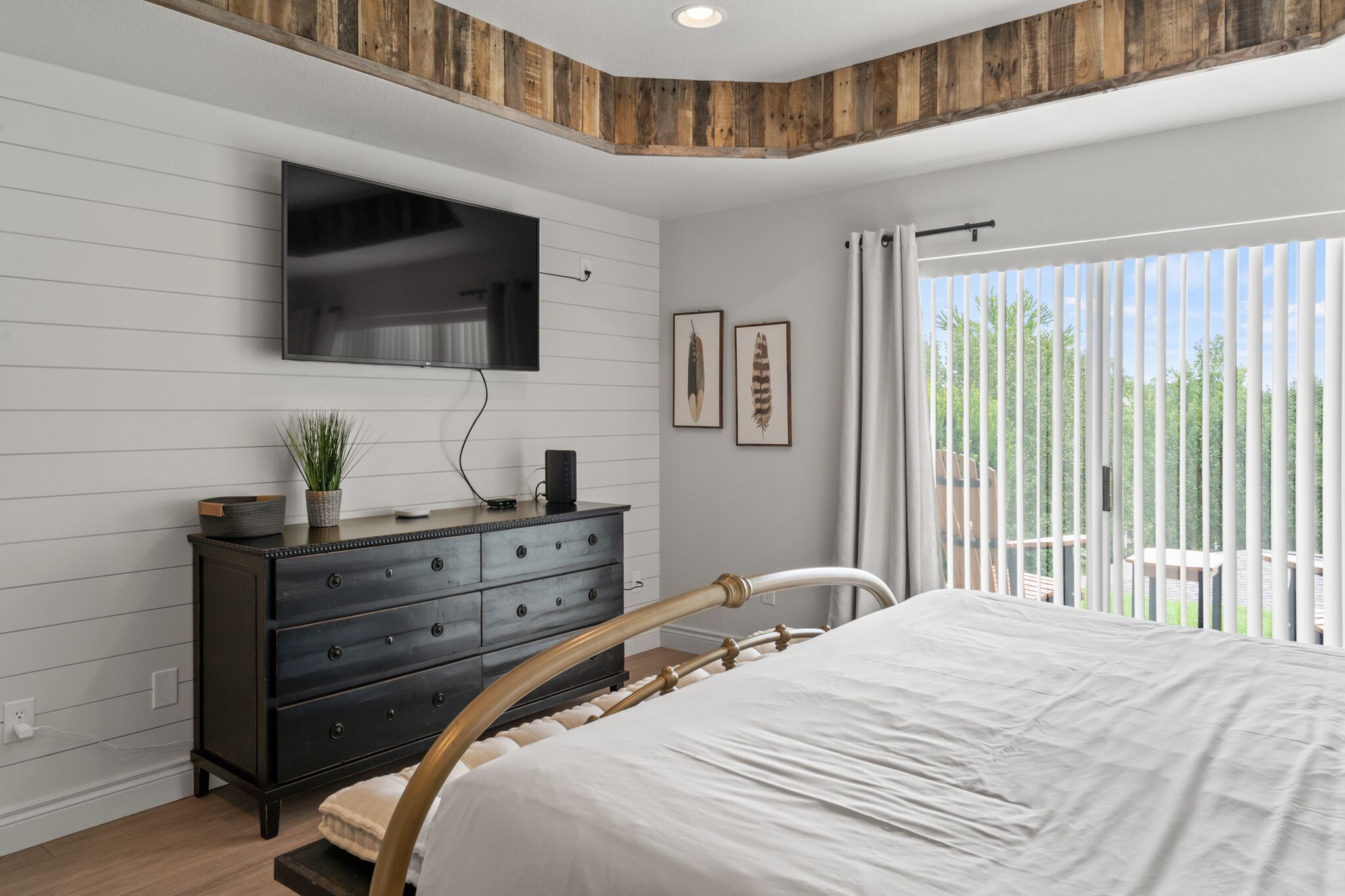 A bedroom with a bed, a dresser, a flat-screen TV, and a window with curtains.