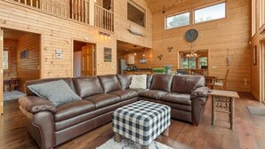 Ein geräumiges Wohnzimmer mit einem großen, braunen Ledersofa, einem karierten Hocker und einem Holzessttisch.