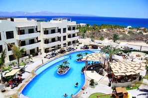 Un resort con una piscina grande, varias edificaciones y vista al mar.