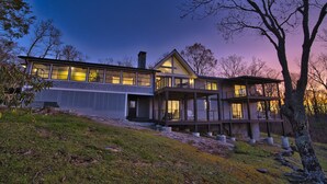 Une maison moderne à deux étages, dotée de grandes fenêtres et d’un balcon, entourée d’arbres et d’une pelouse.
