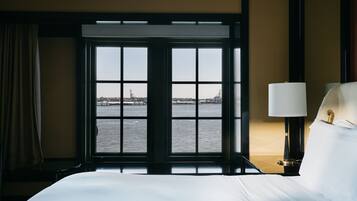 A hotel room with a large window offering a view of the water and distant cityscape.