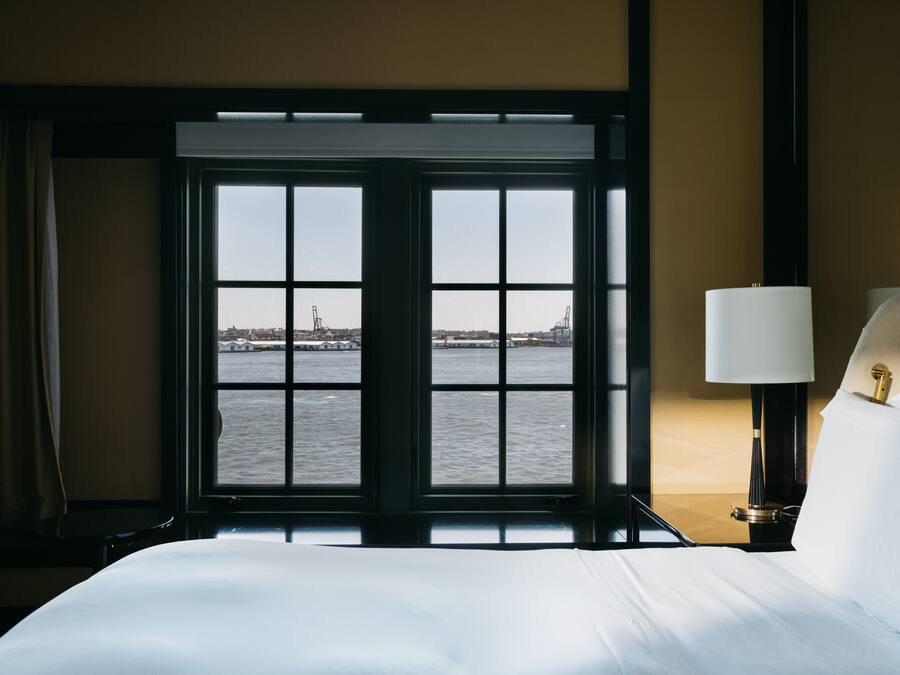A hotel room with a large window offering a view of the water and distant cityscape.