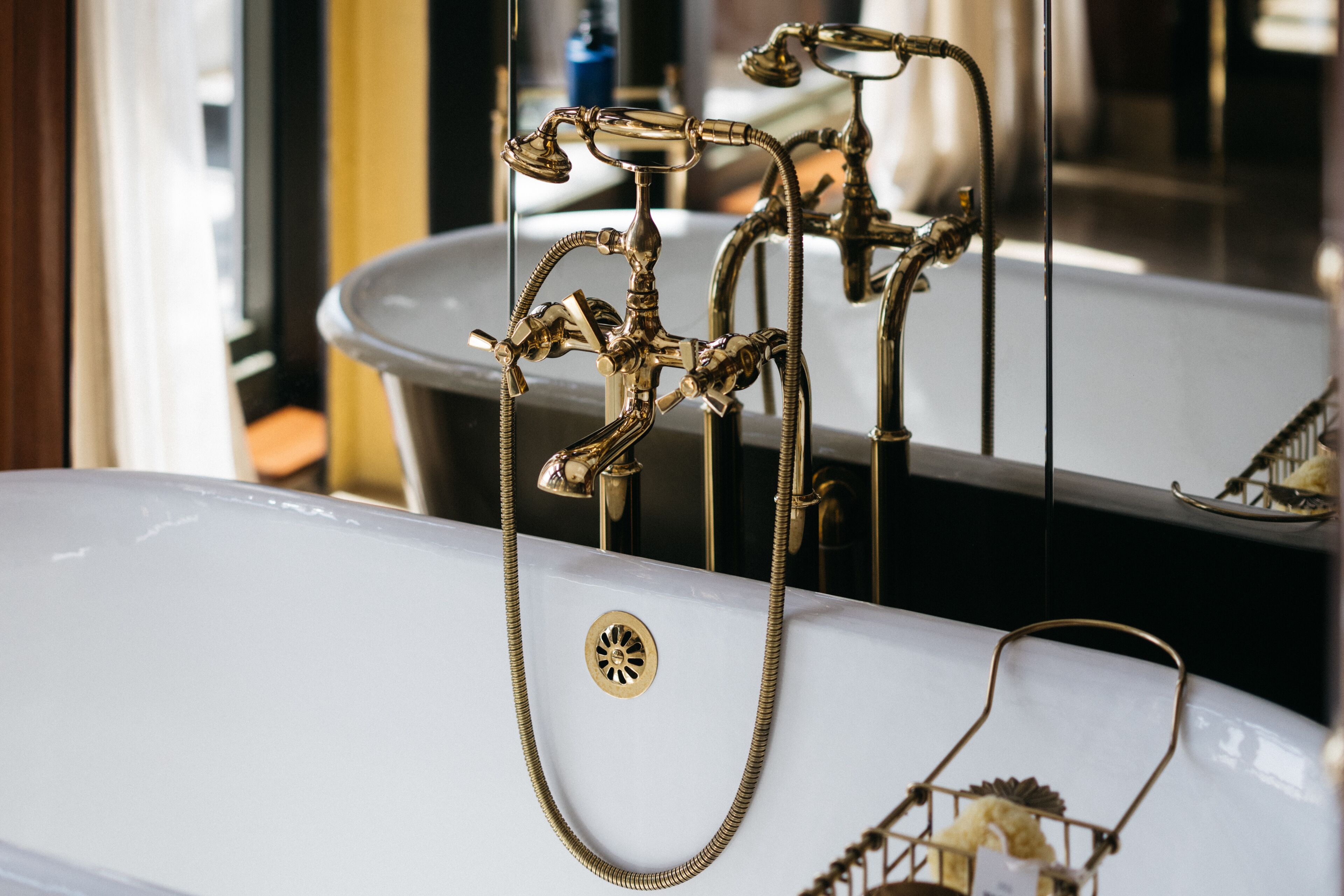 Une baignoire blanche avec un robinet et une pomme de douche dorés, ainsi qu’une chaîne en or.