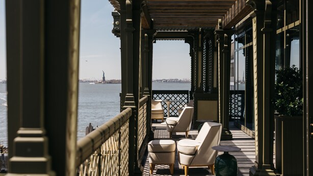 Een balkon met zitplaatsen buiten, uitzicht op het water en een verre stadslijn.